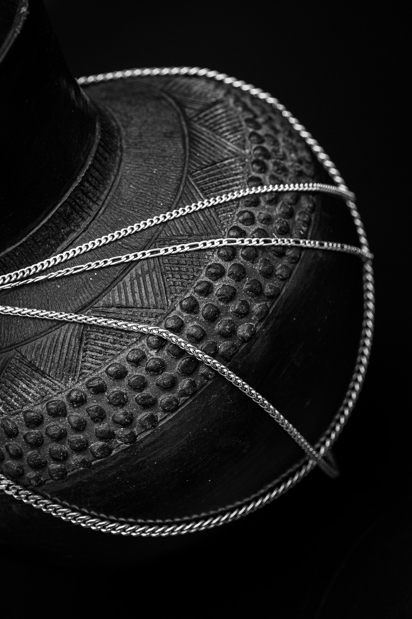 Figaro, wheat, and Cuban chain necklaces in a monochrome image on a black background