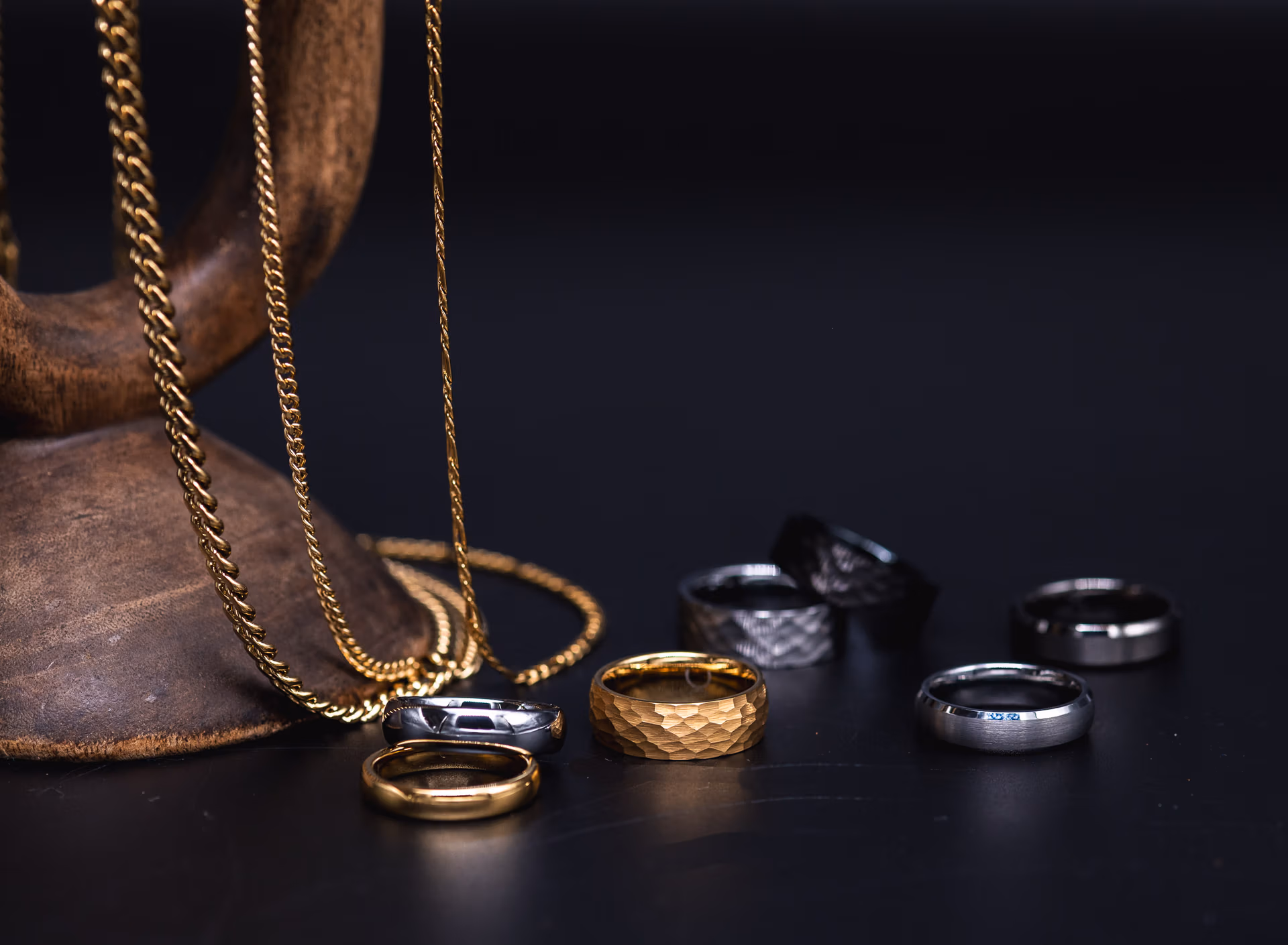 Tungsten rings and gold and silver Cuban chain displayed on wood against a black background